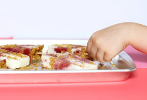 Frozen yogurt pops on a baking sheet with child's hand reaching for one.