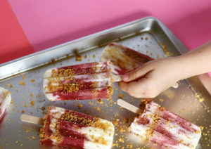 Frozen pops on a baking sheet, with hand holding one.